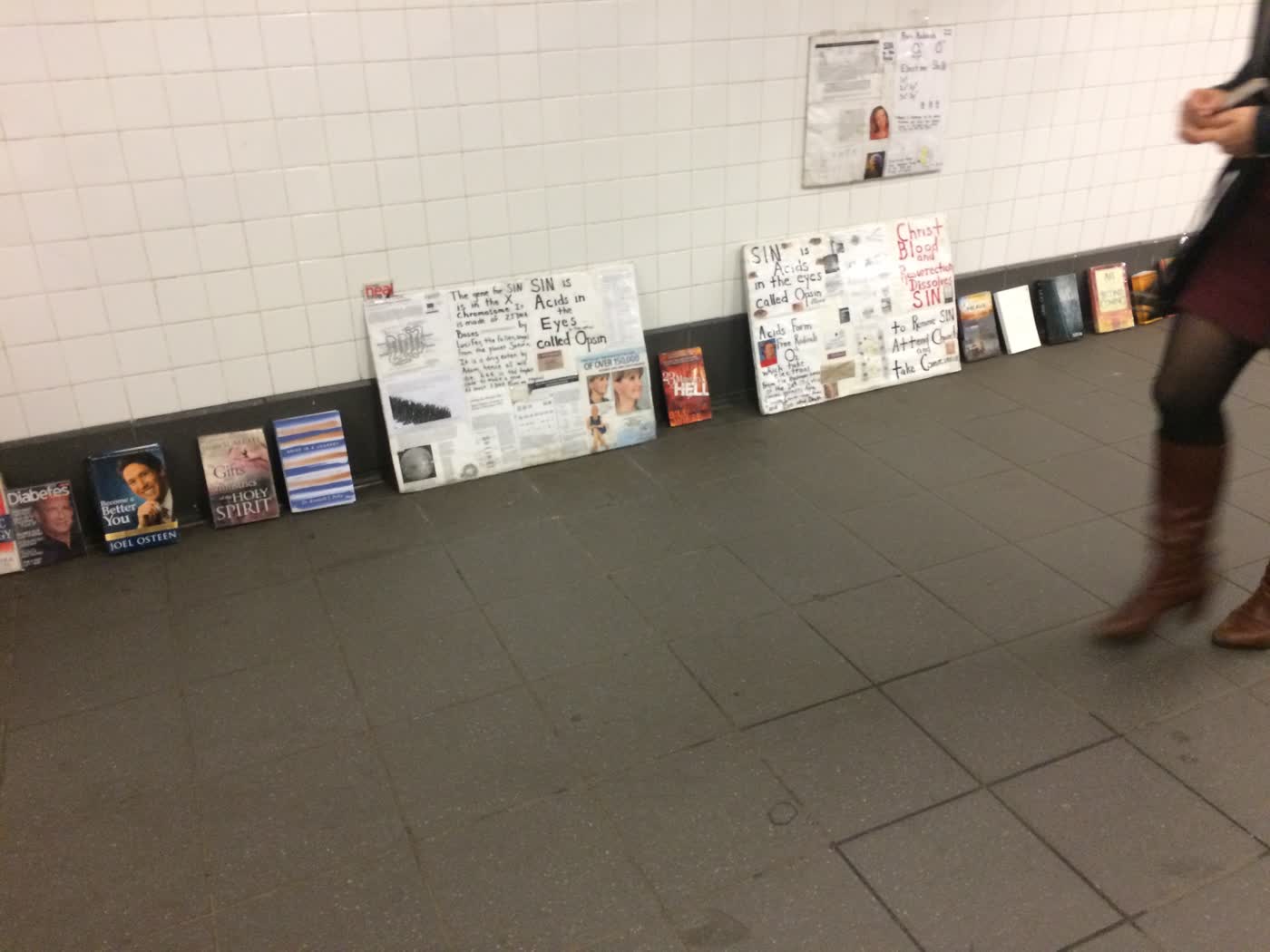 A bunch of signs and books resting up against a wall in the NYC subway.